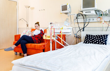 Frau mit Neugeborenem im Arm im Familienzimmer der Neonatologie