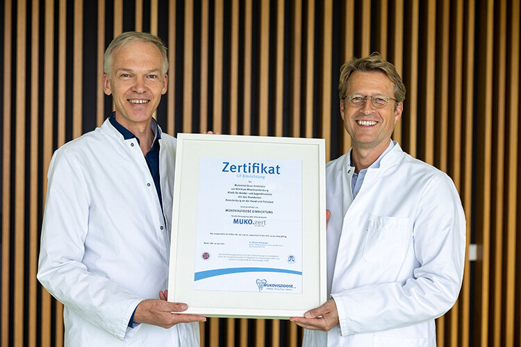 Prof. Dr. med. habil. Jochen G. Mainz und Priv. Doz. Dr. med. Carsten Schwarz zeigen das vom Bundesverband Cystische Fibrose (CF) „Mukoviszidose e.V.“ erteilte Prädikat „Muko.zert Plus“